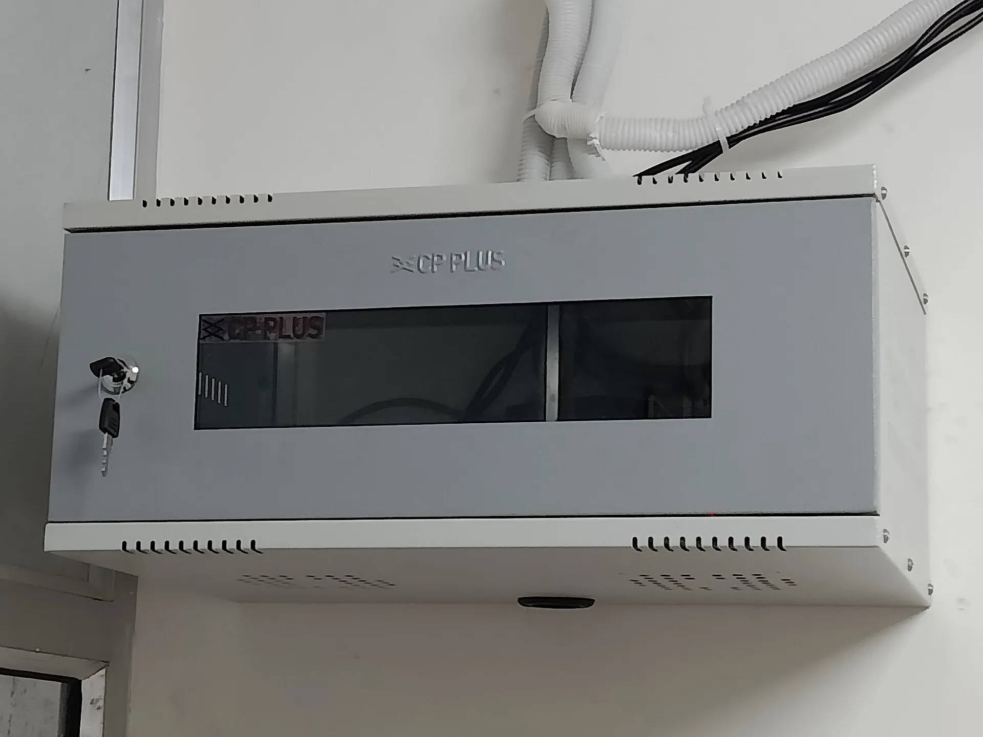 Grey metal wall cabinet with a lock and a ventilated door, with conduit leading in, used to house a recorder