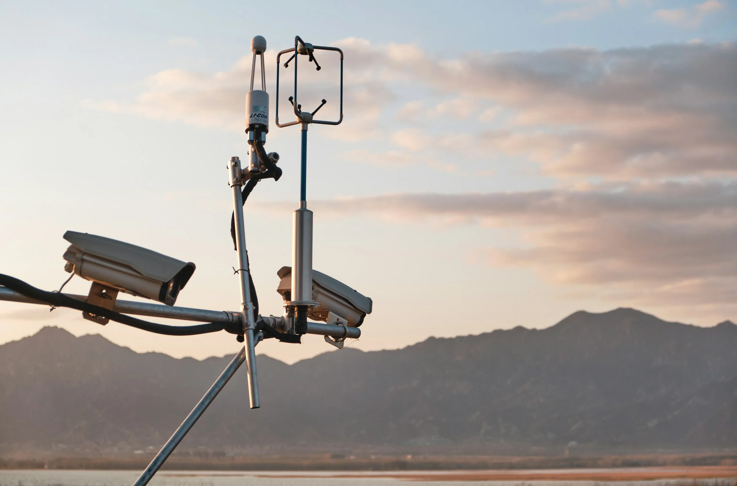 Two security cameras on a mast at dusk, with mountains behind