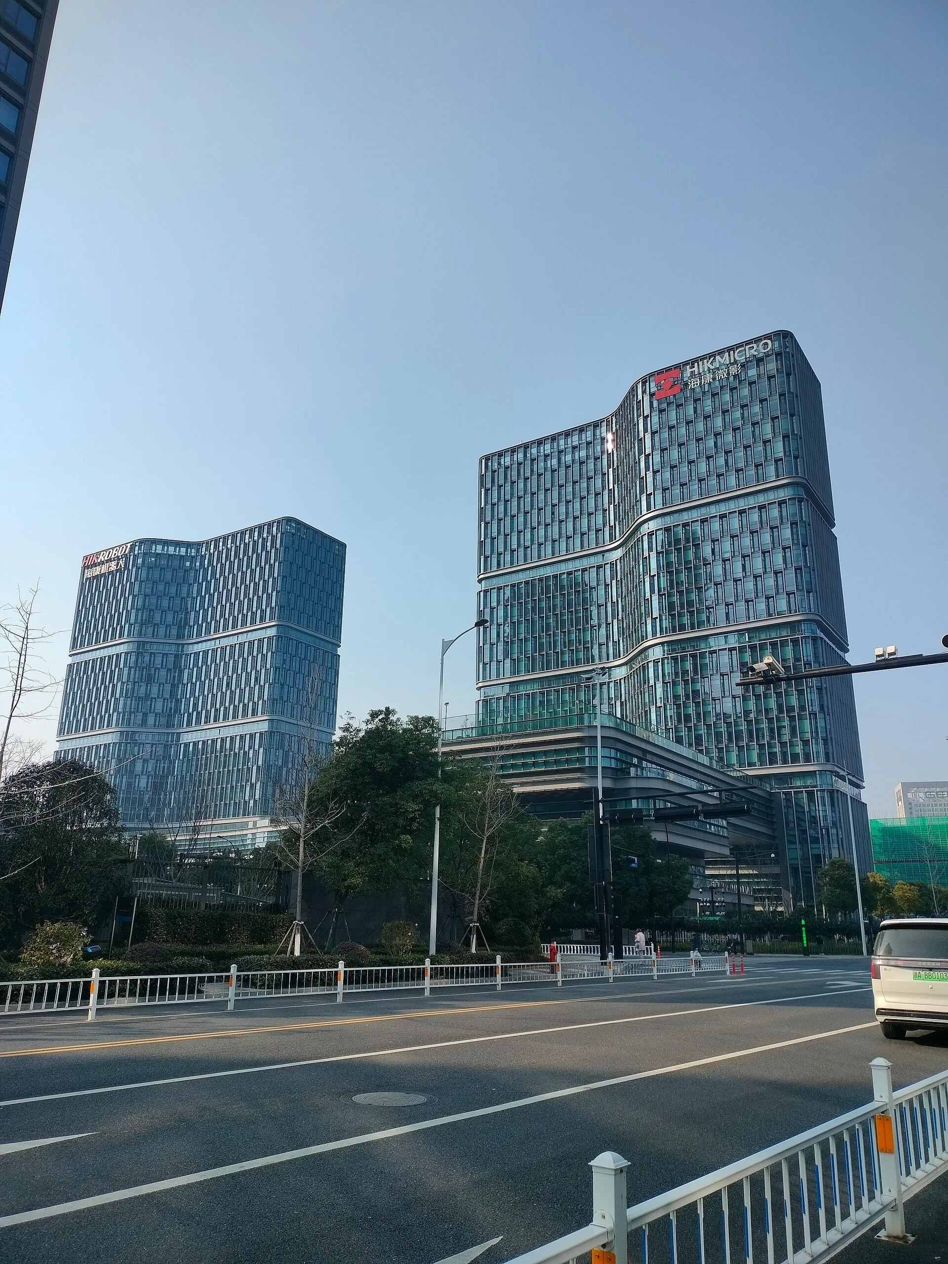 Two tall glass office towers with HikRobot and HikMicro signs on their roofs beside a road