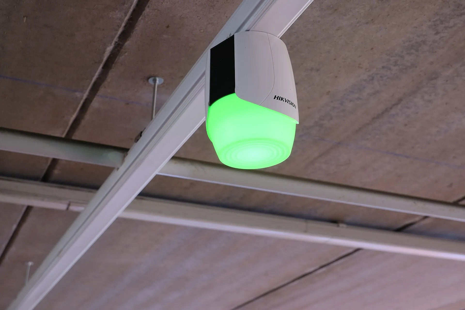 White Hikvision camera hanging from a ceiling rail with a green glowing lower section