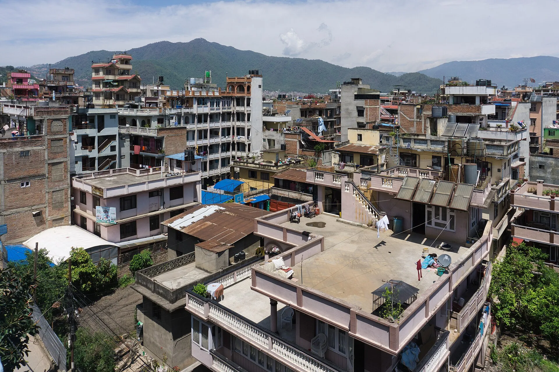 View over flat concrete rooftops, water tanks and solar heaters in Kathmandu with green hills behind