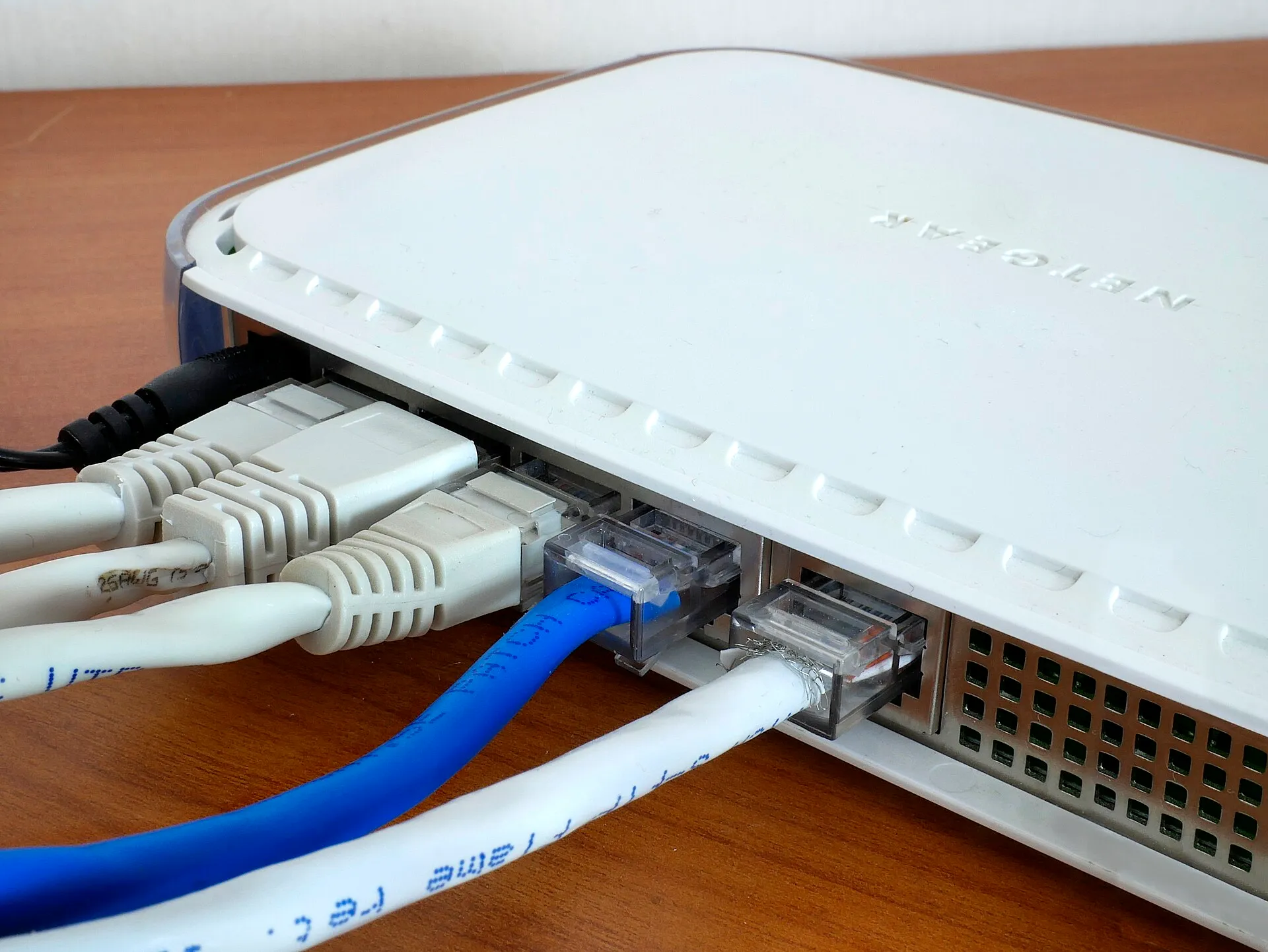 White router with a Netgear label seen from behind with blue, white and grey network cables in its ports