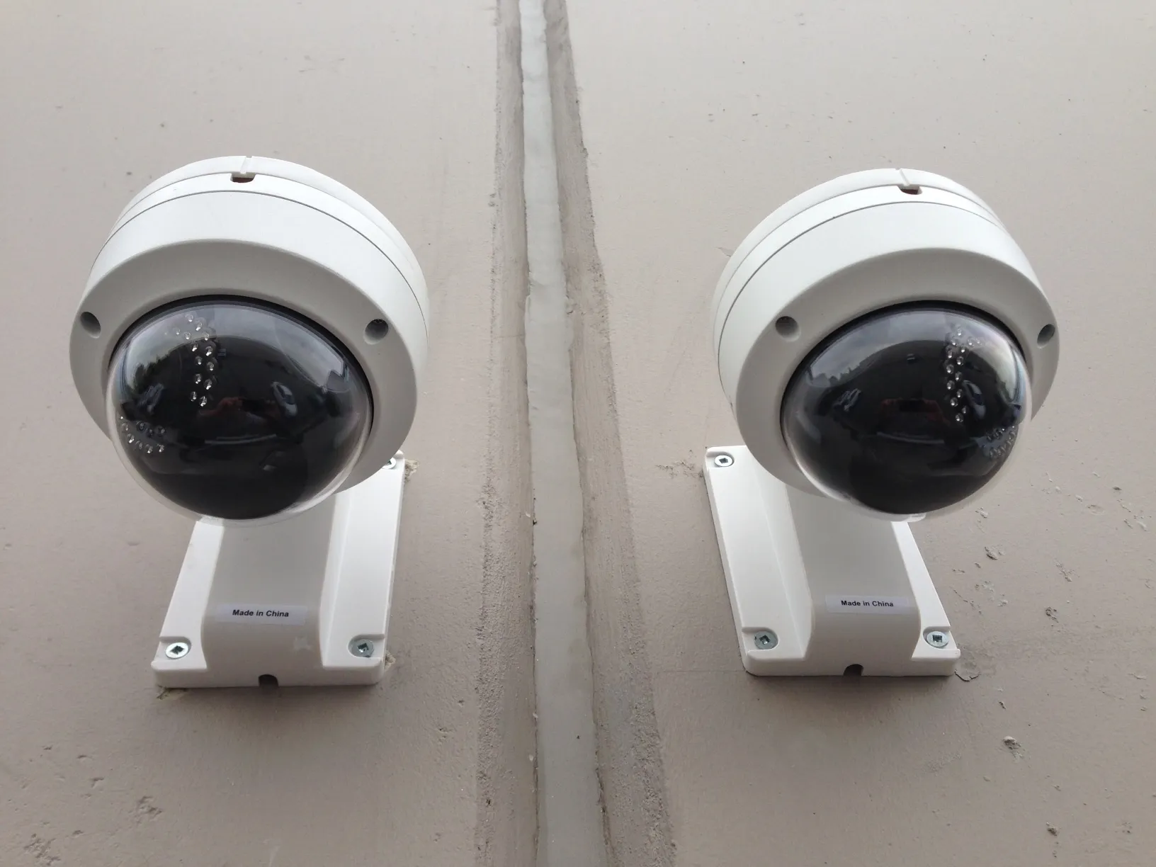 Two white outdoor dome cameras on wall brackets, each with a ring of infrared lights around the lens