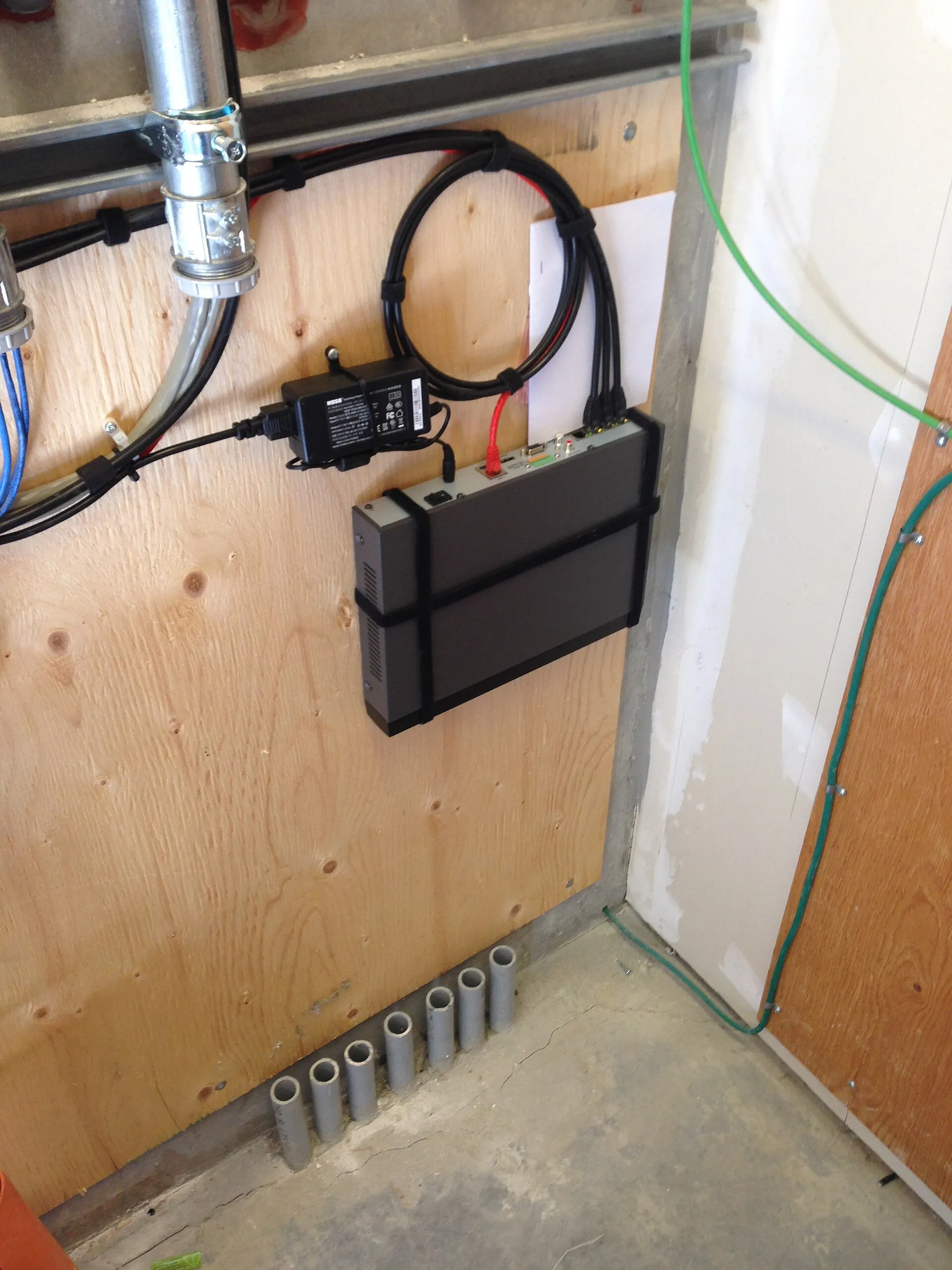 Black recorder mounted on a plywood wall with its cables tied back and a power adapter beside it