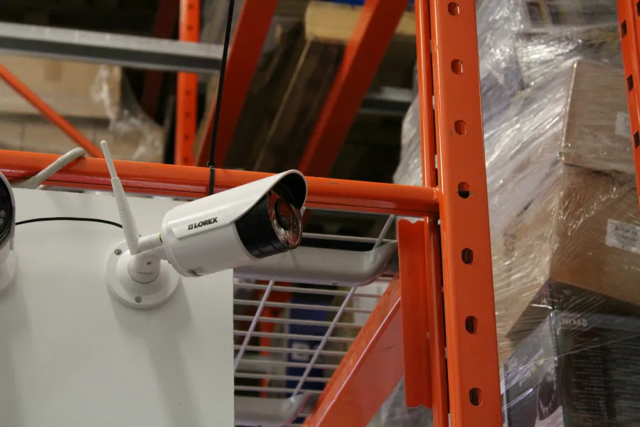 White bullet camera with a small antenna mounted on a warehouse rack